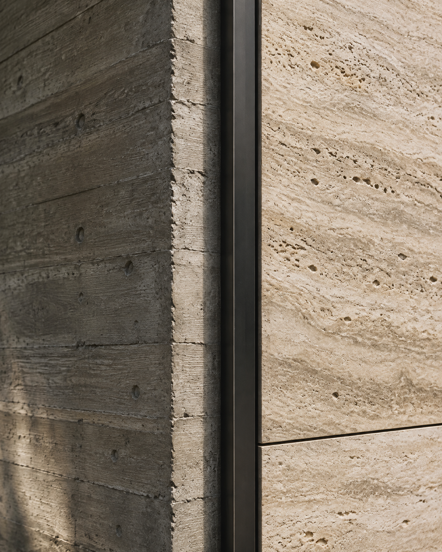 Encontro entre concreto aparente, painel de travertino e perfil metálico